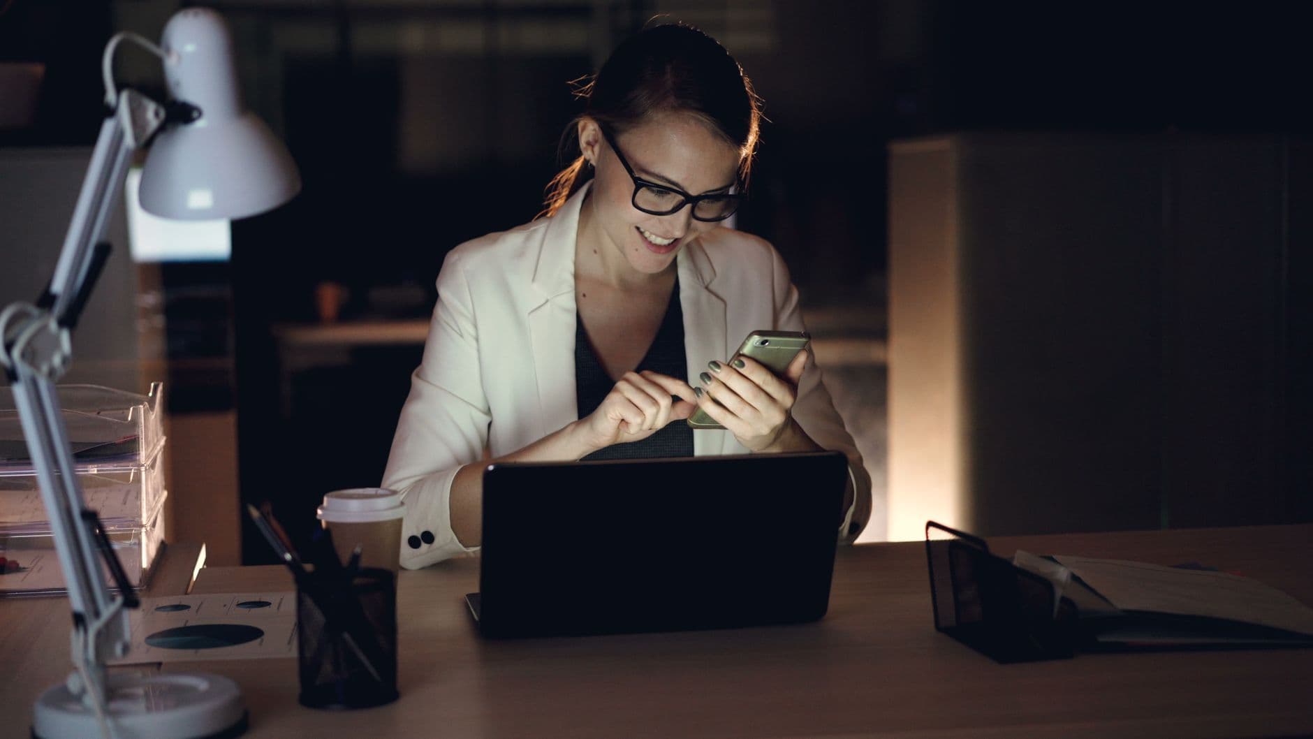A business owner at a desk in the evening, reading something on her phone