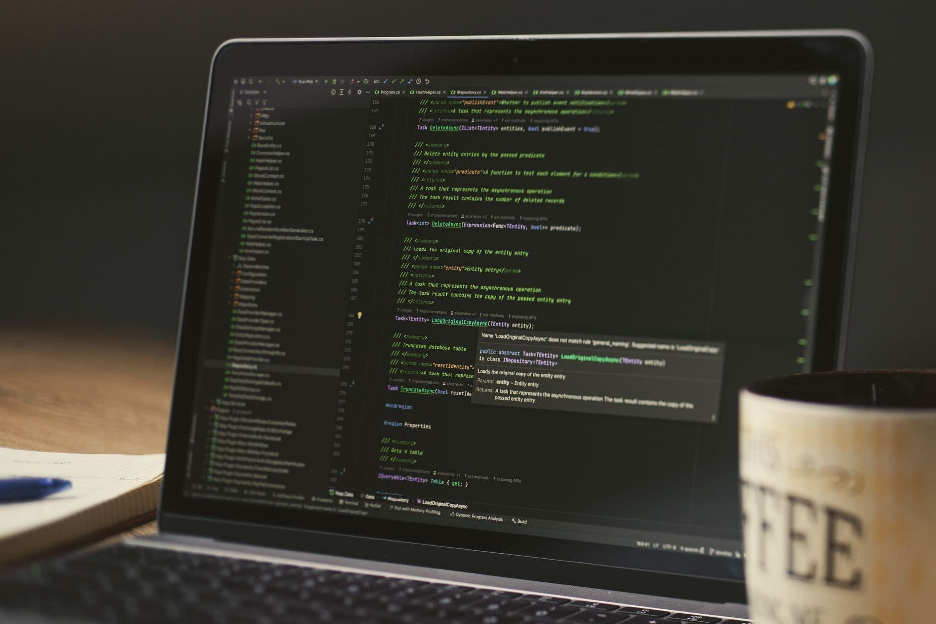A laptop showing code in a dimly lit room beside a coffee mug